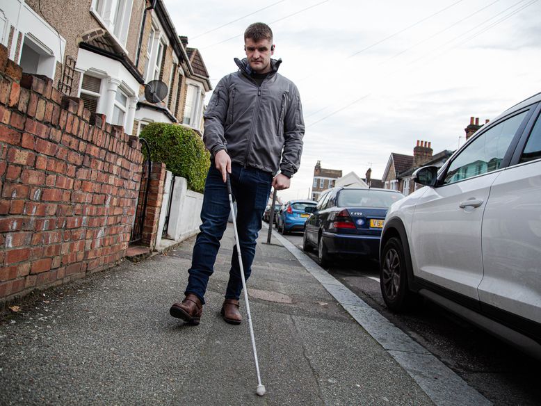 Blind veteran Rob walking on a pavement, using his white cane